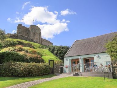 A castle on a hill with a pathway leading to a building with outdoor seating at Tarth Y Mor in Criccieth