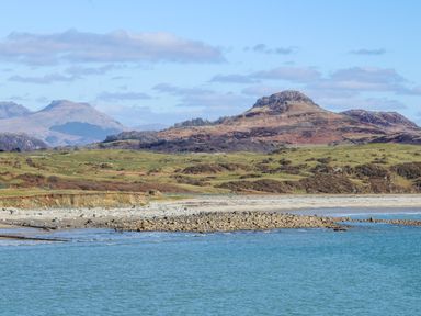 A coastal landscape with a rocky shoreline and hills in the background at Tarth Y Mor in Criccieth