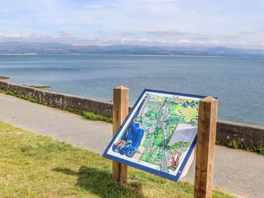 A map board on wooden posts near a pathway by the sea at Tarth Y Mor in Criccieth