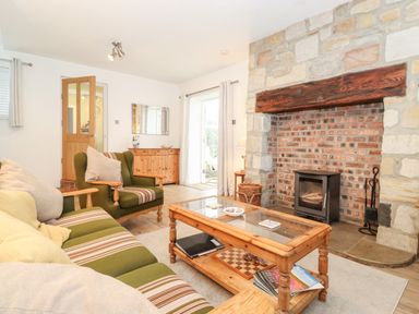 A living room with an armchair and sofa facing a stone fireplace with a wood stove at Canny Cottage Low Hauxley Nr Amble