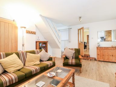A sitting room with a striped green sofa and armchair a wooden coffee table a wooden sideboard and a bookshelf at Canny Cottage Low Hauxley Nr Amble