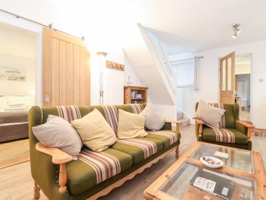 A living room with green striped sofas, a glass coffee table, wooden doors, a staircase, and a bookshelf at Canny Cottage Low Hauxley Nr Amble
