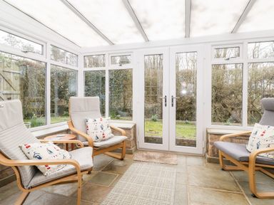 A conservatory with three armchairs a small round table and glass doors overlooking a garden at Canny Cottage Low Hauxley Nr Amble