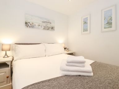 A bedroom with a bed white linens bedside tables with lamps and framed pictures on walls at Canny Cottage Low Hauxley Nr Amble