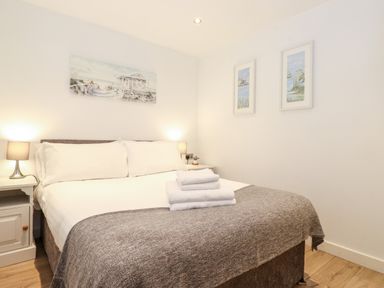A bedroom with a double bed bedside tables lamps folded towels and pictures on the walls at Canny Cottage in Low Hauxley Nr Amble