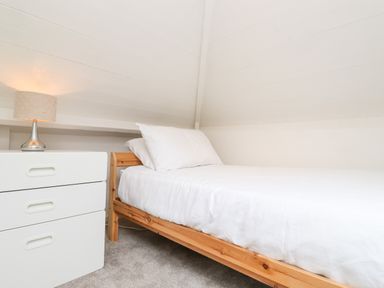 A single bed with white bedding next to a white chest of drawers with a lamp on top at Canny Cottage in Low Hauxley Nr Amble