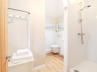A bathroom with a shower, wall-hung toilet, white towels, and a small cabinet at Canny Cottage Low Hauxley Nr Amble