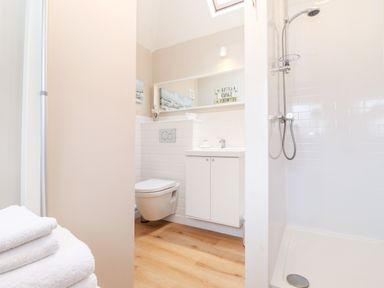 A bathroom with a shower stall wooden floor and white towels at Canny Cottage Low Hauxley Nr Amble