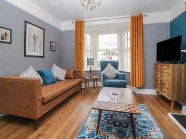 A living room with a brown sofa blue armchair wooden coffee table patterned rug and wooden chest of drawers at Cornerside in Sidmouth