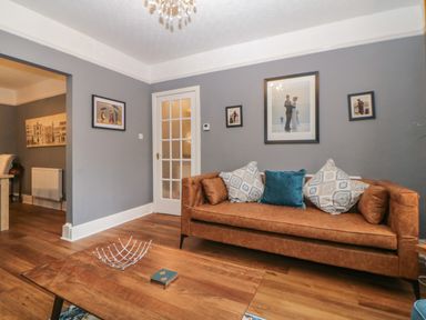 A living room with a brown sofa and cushions a wooden coffee table with a metal centerpiece and wall art at Cornerside in Sidmouth