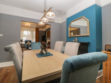 A dining room with a wooden table and upholstered chairs with a large mirror on a blue accent wall at Cornerside in Sidmouth