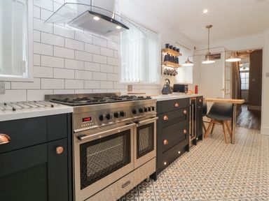 A kitchen with a gas stove oven black cabinets tiled backsplash patterned floor and a small wooden table with chairs at Cornerside in Sidmouth