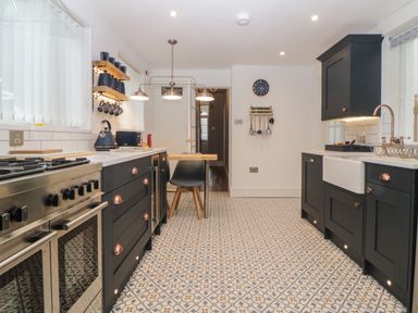 A kitchen with dark cabinets a patterned tiled floor a stainless steel stove and a wall clock at Cornerside in Sidmouth
