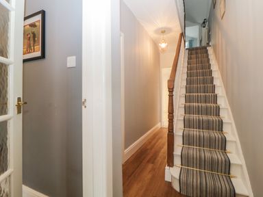 A hallway with wooden flooring and a staircase with a striped carpet runner at Cornerside in Sidmouth