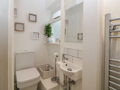 A small bathroom with a toilet a sink a plant on the window sill and framed quotes on the wall at Cornerside in Sidmouth