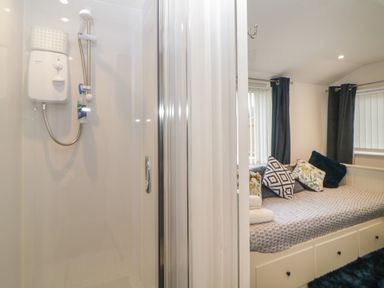 A bathroom shower with a glass door next to a bedroom with a bed and cushions at Cornerside in Sidmouth
