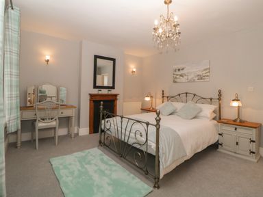 A bedroom with a metal bed frame two bedside tables a wooden dressing table with a chair a mirror and a small fireplace at Cornerside in Sidmouth