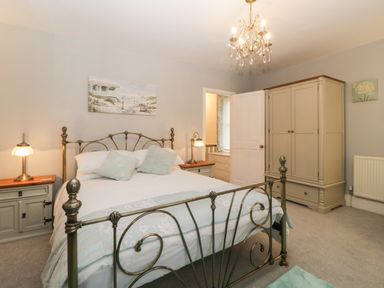 A bedroom with a metal bed frame two bedside tables with lamps a wardrobe and a chandelier at Cornerside in Sidmouth