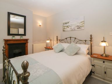 A bedroom with a metal bed frame two bedside tables with lamps a fireplace and a wall mirror at Cornerside in Sidmouth