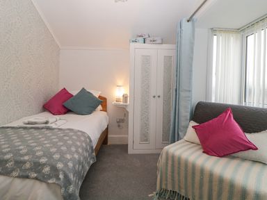 A bedroom with a single bed, wardrobe, and a small sofa near a window at Cornerside in Sidmouth