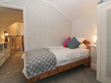 A small bedroom with a single wooden bed two pillows and towels on the bed and a bedside lamp at Cornerside in Sidmouth