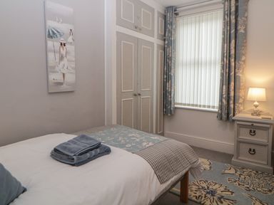 A bedroom with a bed folded towels a nightstand with a lamp a window with curtains and built in closets at Cornerside in Sidmouth