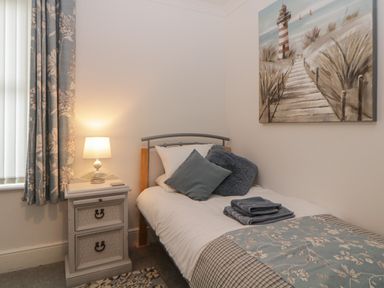 A bedroom with a single bed a bedside table with lamp patterned curtains and a lighthouse painting on the wall at Cornerside in Sidmouth