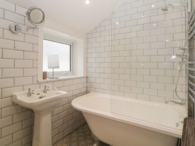 A bathroom with a pedestal sink bathtub tiled walls and a frosted window at Cornerside in Sidmouth