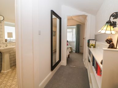 A hallway with a mirror on the wall and a bookshelf with a lamp and books at Cornerside in Sidmouth