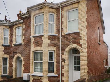 Exterior view of a two story brick house with light and dark bricks and white framed windows at Cornerside in Sidmouth