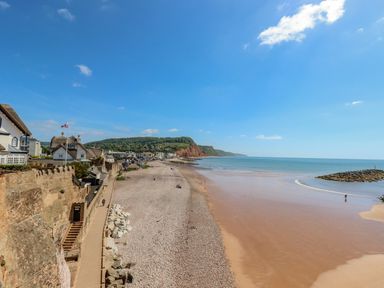 A coastal beach with a pebble and sand shore houses along the promenade and cliffs in the distance at Cornerside Sidmouth