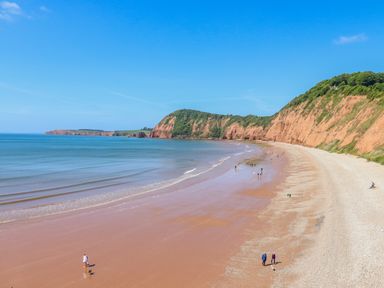 A beach with sandy shore and cliffs along the coastline with people walking and ocean water at Cornerside in Sidmouth