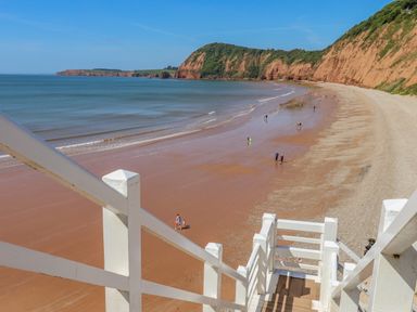 A wooden staircase leading down to a sandy beach with cliffs and people walking along the shore at Cornerside in Sidmouth