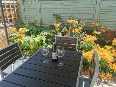 A black outdoor table with two wine glasses and a wine bottle surrounded by orange flowers and green plants at Cornerside in Sidmouth