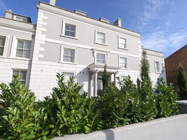 A white multi-story building with columns at the entrance and green bushes in front at 3 Compass Point Weymouth