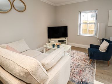 A living room with a beige sofa a blue armchair a white coffee table with cups and plate a television on a white stand two round mirrors on the wall and a window at 3 Compass Point Weymouth
