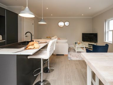 An open plan kitchen and living room with a marble countertop island and white bar stools at 3 Compass Point in Weymouth
