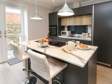 A kitchen with a marble countertop island with two white chairs and fruit bowl at 3 Compass Point in Weymouth