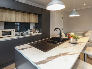 A kitchen with marble countertop island and black sink alongside black cabinets and wooden upper cupboards at 3 Compass Point in Weymouth