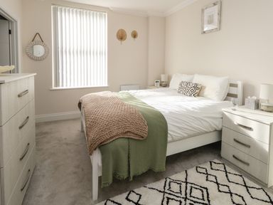 A bedroom with a bed, two bedside tables, a chest of drawers, carpet, and window blinds at 3 Compass Point in Weymouth