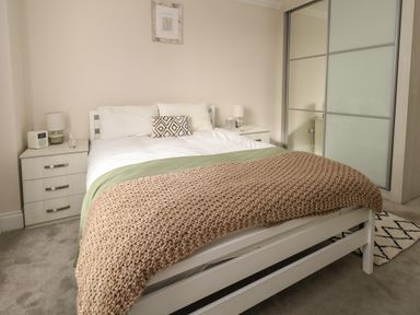 A bedroom with a bed a knitted blanket two bedside tables lamps and a sliding door wardrobe at 3 Compass Point in Weymouth