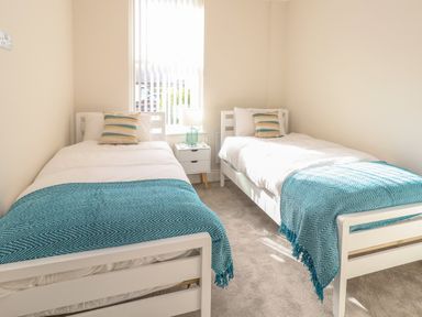A bedroom with two single beds with blue throws and striped pillows at 3 Compass Point in Weymouth
