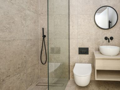 A bathroom with a shower area glass partition wall a toilet a sink with faucet and a round mirror at 3 Compass Point in Weymouth