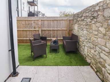 An outdoor patio area with four wicker chairs and a small table on artificial grass surrounded by a stone wall and wooden fence at 3 Compass Point Weymouth