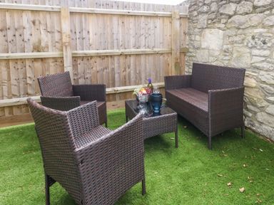 An outdoor seating area with wicker chairs a wicker loveseat a glass top table and a wooden fence at 3 Compass Point in Weymouth
