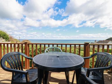 An outdoor wooden deck with a round plastic table and four chairs overlooking the sea at Beachcliff in Gorran Haven