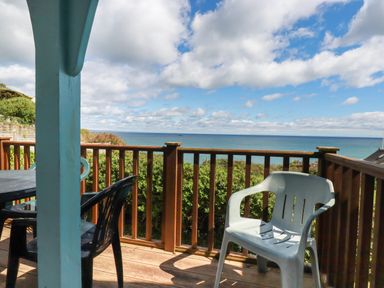 A balcony with plastic chairs and wooden railing overlooking the ocean at Beachcliff in Gorran Haven