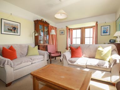A living room with two sofas with cushions a wooden coffee table a wooden cabinet a red chair and framed pictures on the walls at Beachcliff in Gorran Haven