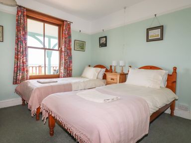 A bedroom with two single beds a wooden nightstand and a window with patterned curtains at Beachcliff in Gorran Haven