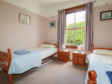 A bedroom with two single beds two wooden nightstands and a window with striped curtains at Beachcliff in Gorran Haven